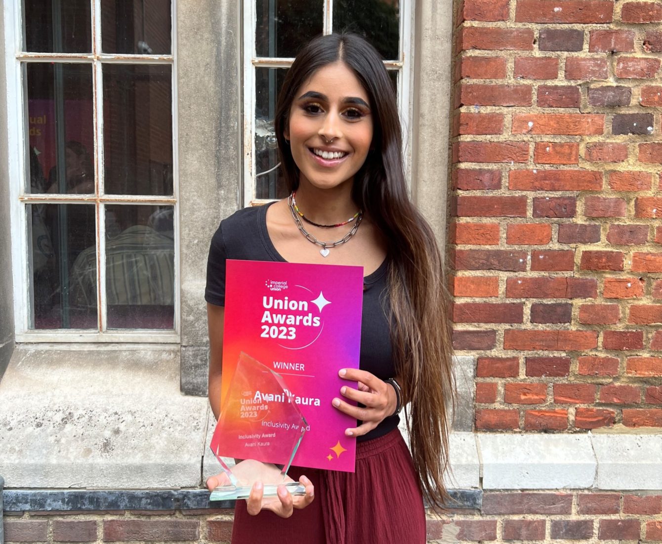 Avi standing in front of a brick building, holding the award and certificate